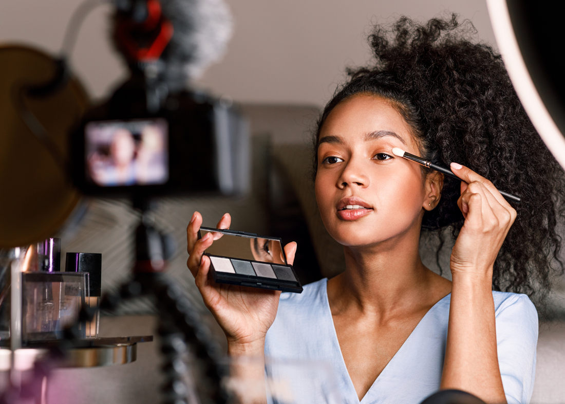 Young Black woman creating beauty content with eyeshadow and ring light. Yany Beauty