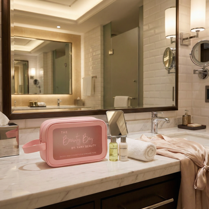 Pink Yany beauty bag on a bathroom counter with skincare products and towels.