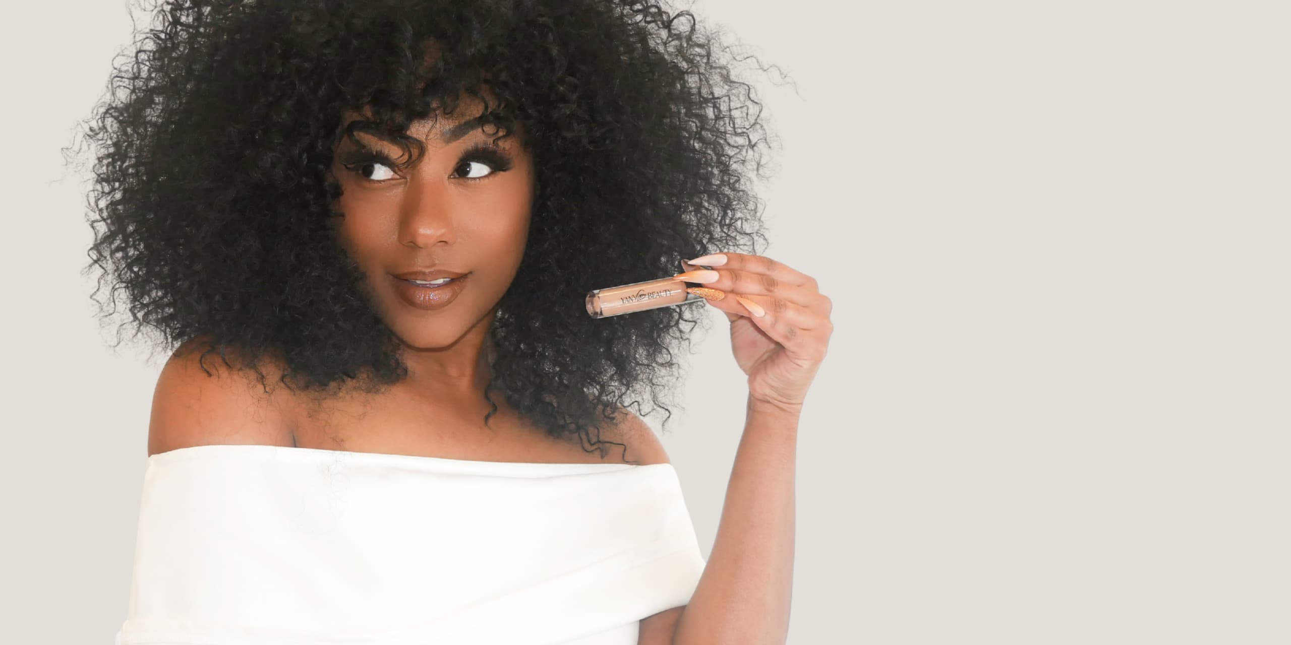 Woman with voluminous hair holding a Yany Beauty full coverage concealer  against a plain background